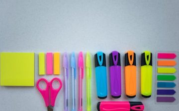 Flat lay of colorful school supplies including pens and highlighters on a white surface.
